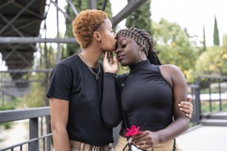 A loving LGBTQ multiethnic couple embraces in a park, sharing a tender moment. One partner gently