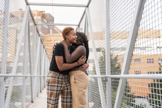 A joyful LGBT multiethnic couple shares a warm embrace on a metal walkway bridge, surrounded by