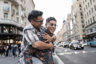 A latin gay couple shares a joyful moment on a bustling street in Madrid, surrounded by beautiful