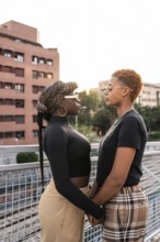 A loving LGBT multiethnic couple stands closely, facing each other, on an outdoor walkway. The