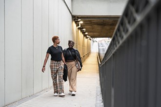 A joyful LGBT multiethnic couple walks side by side through a well-lit urban underpass, sharing a