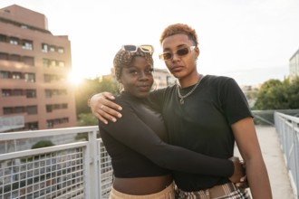 A loving LGBT multiethnic couple embraces outdoors on a bridge during a beautiful sunset. The warm