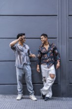 A joyful, stylish latin gay couple shares a lively conversation against a modern urban backdrop.