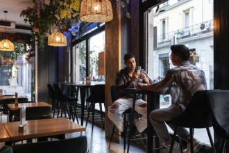 A latin gay couple enjoying a moment in a stylish café, surrounded by chic interior and warm
