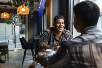 A latin gay couple shares smiles and conversation in a stylish cafe. Warm lighting and contemporary