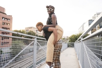 A happy LGBT multiethnic couple enjoys a playful moment on a bridge in an urban setting, with one