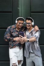 A happy couple in stylish outfits share a joyful moment with headphones and a smartphone. They