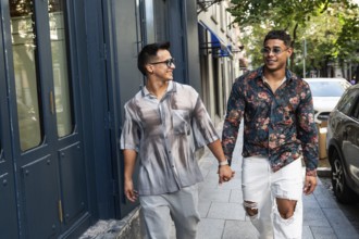A happy latin gay couple holds hands while strolling down a lively city street in Madrid. They wear