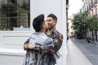 A joyful latin gay couple embraces and shares a tender moment on a charming street in Madrid. The