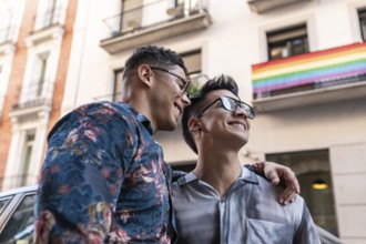A joyful latin gay couple embraces, smiling on the vibrant streets of Madrid. The background