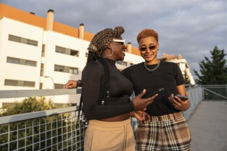 A happy LGBT multiethnic couple smiling while holding phones, enjoying the sunny outdoors in