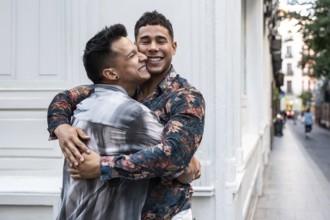 A joyful latin gay couple shares a warm embrace on a charming street in Madrid, reflecting love and