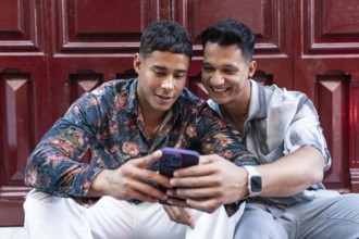 A joyful latin gay couple shares a happy moment in Madrid city. They are sitting together, smiling