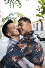 A joyful latin gay couple embraces lovingly on a sunny street in Madrid. The background features