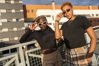A fashionable LGBT multiethnic couple stands on a terrace, basking in the sunlight. One wears plaid