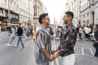 A joyful latin gay couple holds hands and smiles at each other amidst the hustle and bustle of a