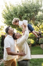 A joyful gay couple playing with their young son in a sunlit garden, capturing a heartwarming,