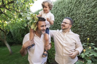 A joyful moment captured outdoors shows a gay couple spending quality time with their young son.
