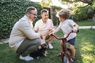 A joyful gay couple engages with their young son in a vibrant green garden, surrounded by lush
