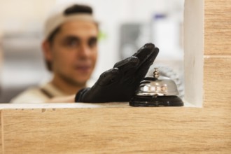 A baker wearing a glove is seen inside an Italian bakery, with a focus on a service bell on the