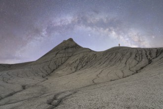 Unrecognizable lone figure stands atop a rugged hill under the starry sky of the Milky Way in the