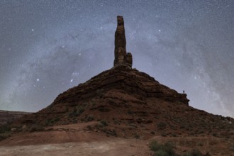 Unrecognizable silhouette of a person standing on a massive rock formation under the starry sky of