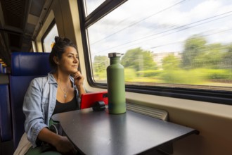 A thoughtful passenger gazes out a train window, absorbing the scenic landscape Sunlight filters