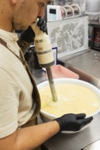 A skilled baker uses an immersion blender to prepare batter in a large bowl The setting is a