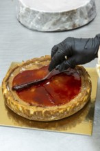 A baker wearing black gloves skillfully spreads glossy red glaze over a freshly baked tart The tart