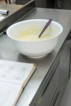 A mixing bowl with batter and a purple spatula on a stainless steel counter, next to an open recipe
