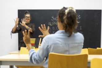 A sign language instructor teaches a student in a classroom The student mirrors hand gestures while