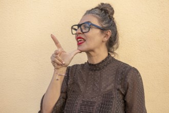 A woman with glasses and a stylish blouse demonstrates sign language with expressive gestures and a