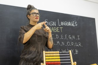 An instructor teaching sign language in a classroom, standing in front of a chalkboard with the