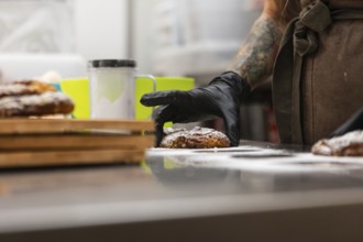 A skilled baker with tattooed arms wearing gloves arranges freshly baked pastries on a counter The