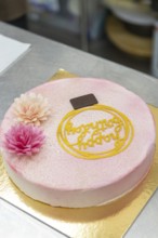 A beautifully decorated Italian cake with pink floral accents, a chocolate square, and an ornate