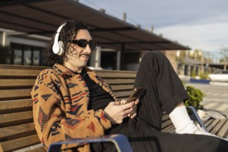 A man relaxes on a bench, wearing headphones and sunglasses, enjoying music on a sunny day He wears