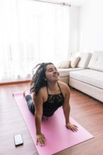 A young latin woman performs yoga on a pink mat in her cozy living room, enjoying a peaceful moment