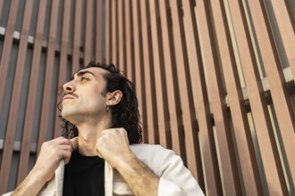 A man gazes upward with confidence, adjusting his collar against a modern architectural backdrop