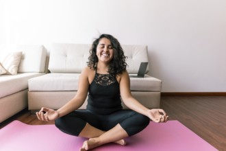 A young latin woman sits peacefully on a yoga mat in a serene living room She practices yoga,