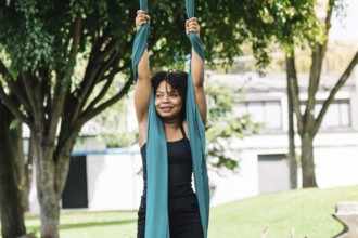 A black performer practices aerial gymnastics on fabric in a vibrant Bogota park, surrounded by