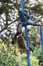 Aerial gymnast performs acrobatics on blue silk fabric amidst lush greenery in a Bogota park The