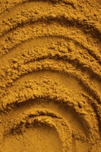 A vibrant close-up of golden curry powder, showcasing its textured surface with swirling patterns