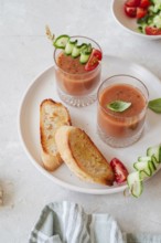 Two glasses of refreshing gazpacho are garnished with cucumber and tomato skewers, accompanied by