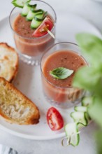 Two glasses of gazpacho topped with cucumber and tomato skewers, alongside toasted bread, served on