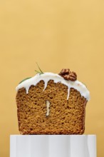 A mouthwatering carrot cake loaf with creamy white frosting sits against a warm orange background