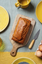 A freshly baked carrot cake loaf sits on a wooden board surrounded by a warm, autumn-themed table
