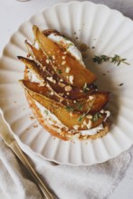 Top view of a gourmet pear toast topped with sliced pears, crumbled cheese, honey drizzle, and