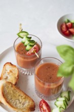 Two glasses of gazpacho garnished with cucumber and tomato skewers, served with toasted bread A