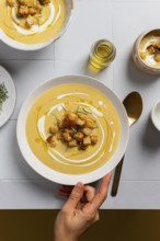 A creamy cauliflower curry soup garnished with croutons, rosemary, and drizzles of cream, served in