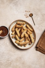 Top view of a ceramic plate filled with homemade churros, coated with sugar and cinnamon,